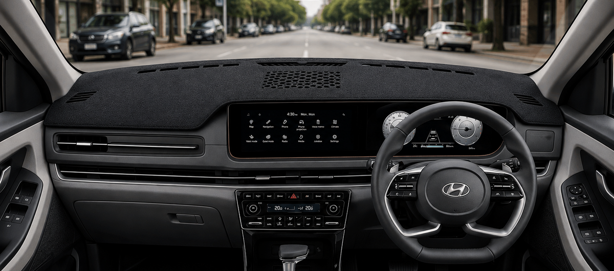 A clean, front-facing view of a modern car interior, showing the dashboard, steering wheel with a Hyundai logo, center console, and gray fabric seats. The car is parked on a city street with trees and buildings visible through the windshield.